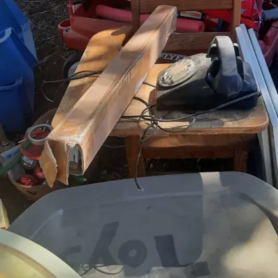 Vintage black rotary phone sitting on a small wooden child's chair alongside outdoor play equipment and storage containers.