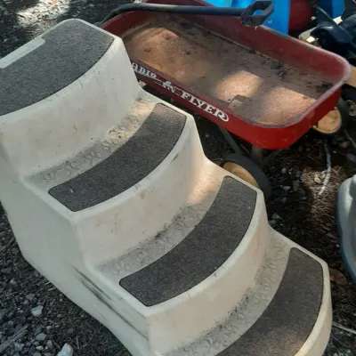 Molded plastic four-step pet stairs alongside a vintage red Radio Flyer wagon and colorful children's activity toys outdoors.