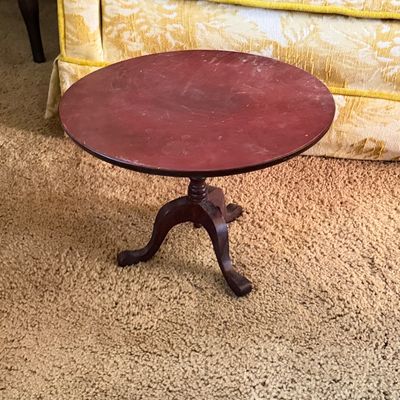 Small wooden pedestal side table with a round top and tripod base, featuring visible surface wear and scuffs.