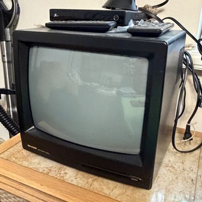 Vintage Sharp CRT television in a black casing, topped with a digital converter box, antenna, and remotes.