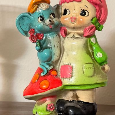 Vintage 1970s ceramic figurine featuring a girl with pink hair standing next to a blue mouse on a mushroom, displaying some age-related...