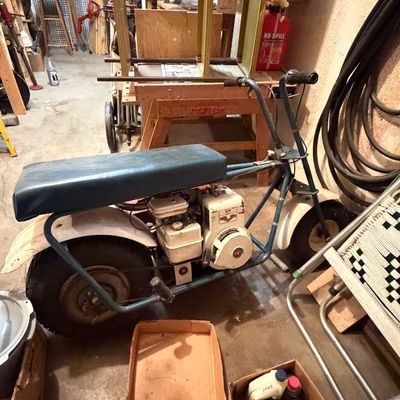 Vintage mini bike featuring a blue tubular frame, padded vinyl seat, white fenders, and a small Tecumseh gas engine, surrounded by...