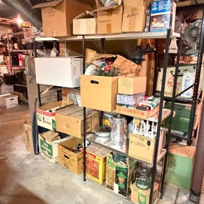 Metal industrial shelving unit filled with organized cardboard storage boxes, vintage hardware supplies, and household items in a...