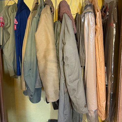 Collection of vintage military outerwear and garments hanging in a closet, including field jackets, coats with faux-fur collars, and...