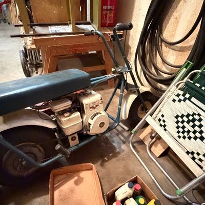 Vintage blue mini bike with a Tecumseh engine, alongside a stack of aluminum webbed folding lawn chairs.