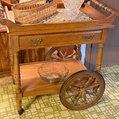 Vintage oak tea cart featuring large spoked wooden wheels, a single drawer, and turned legs, display-ready with cut crystal bowls and...