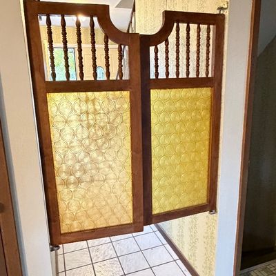 Vintage wood and textured amber glass swinging cafe doors mounted in a doorway, featuring turned spindle accents.