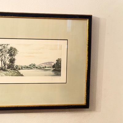 Framed landscape etching depicting a tranquil river scene, double-matted in a black and gold trim frame.