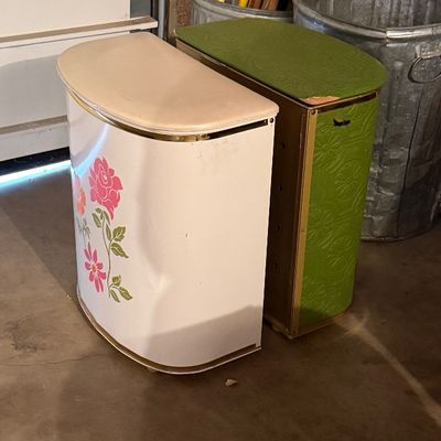 Pair of vintage mid-century hampers with padded tops, including a white vinyl hamper with floral decal and an avocado green embossed...