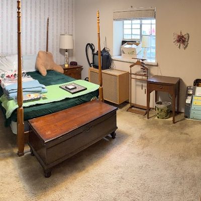 Bedroom filled with vintage furniture, including a four-poster bed frame, wooden trunk, large wall mirror, painted chest of drawers, and...