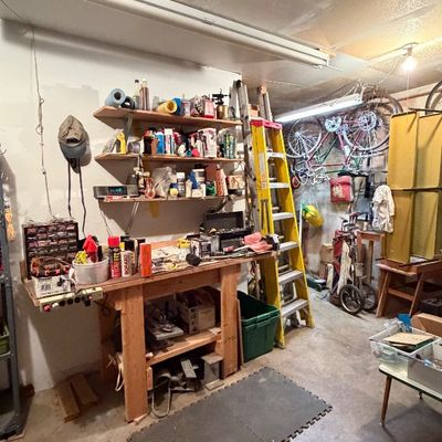 Workshop and garage area featuring a wooden workbench, wall-mounted shelving, extension ladders, hanging bicycles, and assorted tools and...