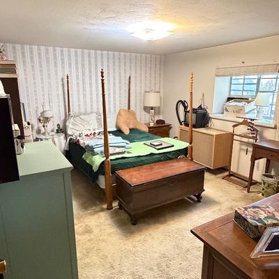 Vintage four-poster bed frame paired with a wooden storage chest at the foot, surrounded by assorted bedroom furniture including a green...