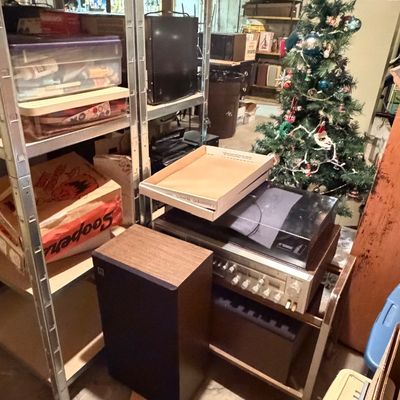 Vintage stereo equipment including a receiver, turntable, and wooden cabinet speaker, arranged on a cart and nearby shelving units in a...
