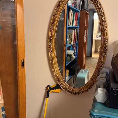Vintage oval wall mirror with an ornate gilt frame, styled with a raised floral motif along the edge.