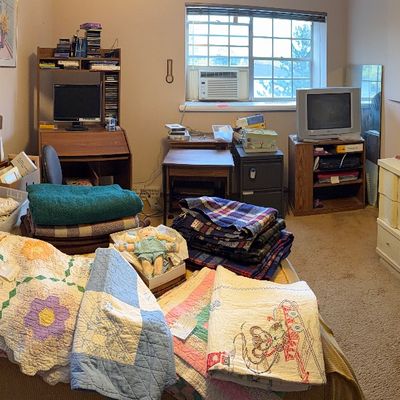 Bedroom filled with vintage textiles, handmade quilts, and blankets displayed on the bed alongside mid-century furniture, including a...