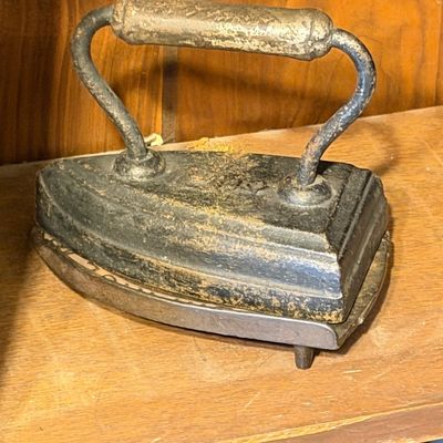 Antique cast iron sad iron resting on a metal trivet, displaying surface wear and aged patina.