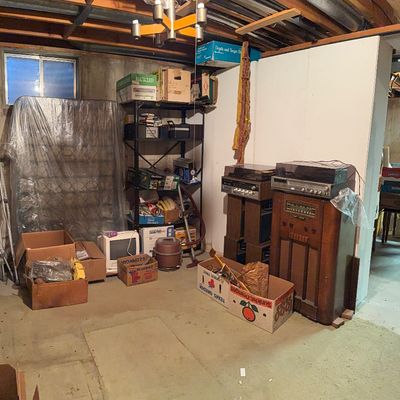 Unfinished basement area featuring vintage electronics, including a floor-standing console radio and stereo components, alongside metal...
