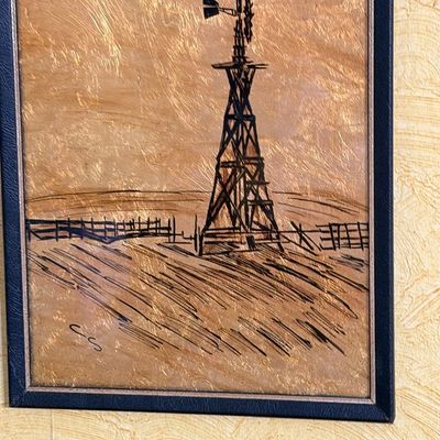 Framed rustic landscape artwork depicting a windmill and fence, executed with ink or pyrography on a textured metallic gold background.