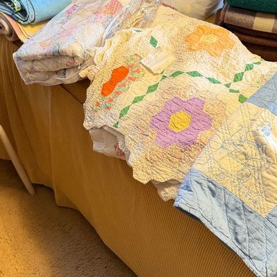 Collection of handmade vintage quilts and blankets laid out on a table, including a floral grandmother's flower garden design and...