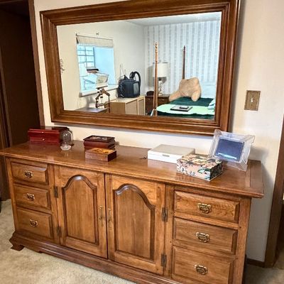 Large wooden triple dresser with matching framed wall mirror, featuring panel doors, multiple drawers, and brass bail handles.