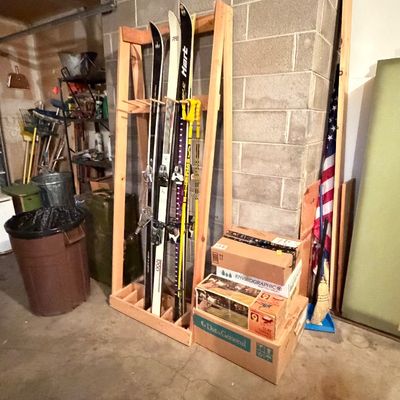 Wooden ski rack holding several pairs of vintage skis and poles, next to stacked cardboard storage boxes in a garage setting.
