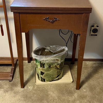 Vintage wood sewing machine cabinet with a faux drawer front and metal pull, featuring slight scuffing on the legs.