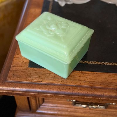 Vintage jadeite glass rectangular trinket box with embossed rose motif lid resting on a wooden desk.