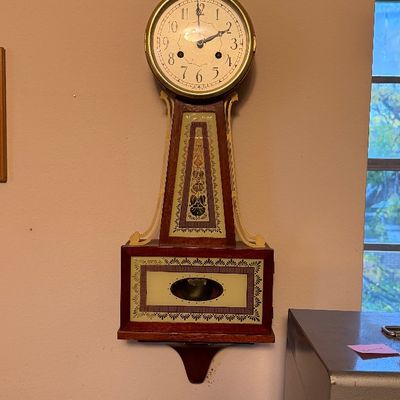 Vintage banjo-style wall clock featuring a mahogany case with decorative stenciled glass panels and a brass eagle finial.