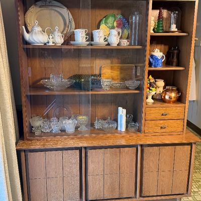 Mid-century modern oak china hutch featuring sliding glass doors, side display shelving, small drawers, and lower cabinet storage filled...