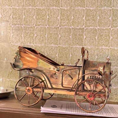 Vintage metal model of an early 20th-century antique automobile, featuring copper and brass tones with intricate spoke wheels.