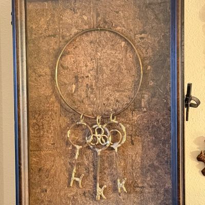 Framed shadow box wall display featuring a set of three decorative metal keys suspended from a large metal ring against a textured...