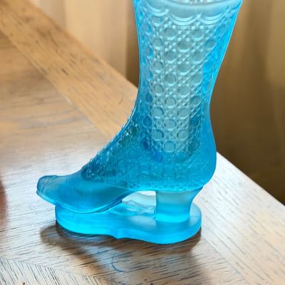 Vintage light blue pressed glass boot figurine with a cane pattern and scalloped rim, displayed on a wooden surface.