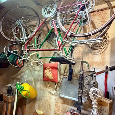 Vintage road bicycles hanging from ceiling hooks in a workshop, surrounded by golf clubs, hand tools, and garage storage items.