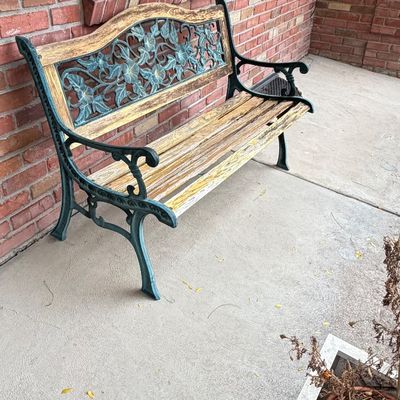Outdoor garden bench featuring weathered wood slatted seating and green verdigris cast metal arms and backplate with floral scrollwork.