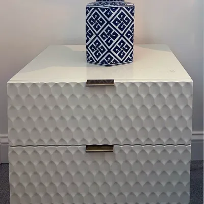 Sale Photo Thumbnail #210: Modern white two-drawer nightstand featuring textured dimpled drawer fronts, metal lip pulls, and slender legs, topped with a blue and white geometric ceramic table lamp.