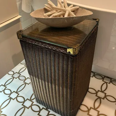 Sale Photo Thumbnail #178: Tall dark woven wicker hamper featuring brass corner accents and a glass top, topped with a decorative textured bowl filled with dried starfish.