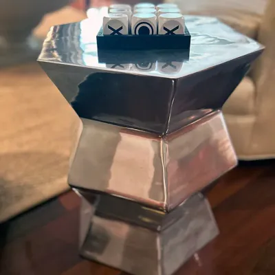 Sale Photo Thumbnail #85: Modern polished metal geometric side table featuring an hour-glass faceted structure, topped with a decorative tic-tac-toe game set.