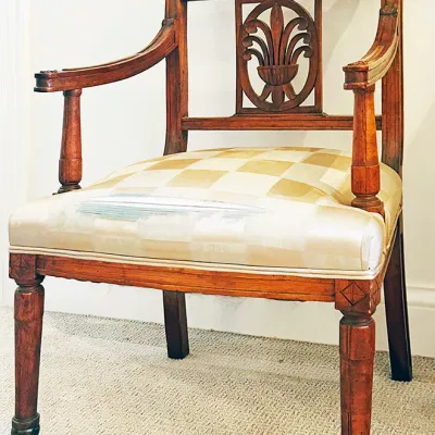 Sale Photo Thumbnail #185: Antique carved wooden armchair featuring an ornate top crest rail, central splat motif, and a checkered upholstered seat with visible wear.