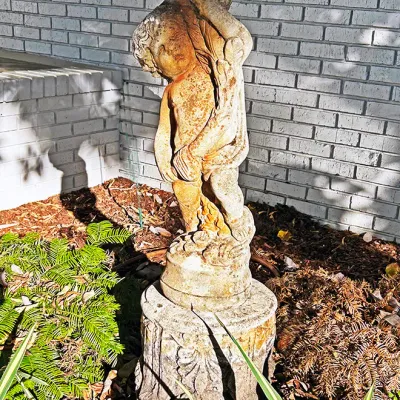 Sale Photo Thumbnail #226: Weathered concrete garden statue birdbath featuring a cherub or putto holding a scalloped basin, set on a fluted pedestal base.