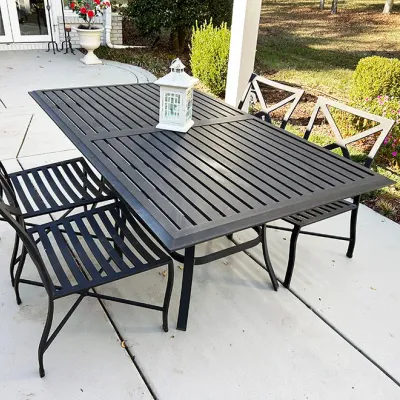 Sale Photo Thumbnail #219: Black metal outdoor patio dining set, including a slatted rectangular table and four matching chairs, accompanied by a decorative white lantern centerpiece.