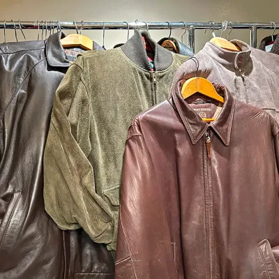 Sale Photo Thumbnail #299: Selection of vintage men's leather and suede jackets hanging on a clothing rack, including a Tommy Hilfiger leather jacket.