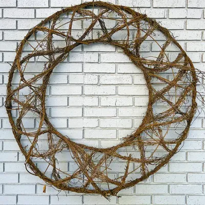 Sale Photo Thumbnail #222: Large circular woven grapevine wall decor hanging against a painted white brick background.