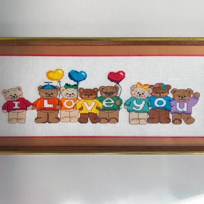 Sale Photo Thumbnail #27: Framed cross-stitch art featuring teddy bears spelling out "I Love You" on colorful sweaters, housed in a wood and gold-tone frame.