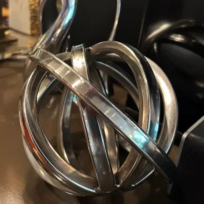 Sale Photo Thumbnail #71: Modernist polished metal armillary sphere paperweight sculpture alongside a stylized silver swan figurine.