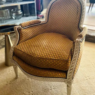 Sale Photo Thumbnail #147: French Louis XVI style painted bergère armchair featuring a carved whitewashed wood frame and gold patterned upholstery.