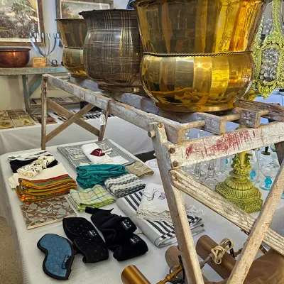 Sale Photo Thumbnail #276: Selection of estate sale items including polished brass planters displayed on a vintage wooden ladder, folded linens, and brass picture lights.