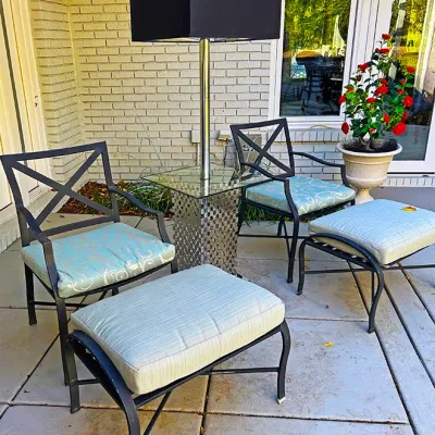Sale Photo Thumbnail #221: Pair of black metal patio armchairs with matching ottomans and patterned light blue cushions, arranged alongside a chrome floor lamp featuring an integrated glass-top accent table.