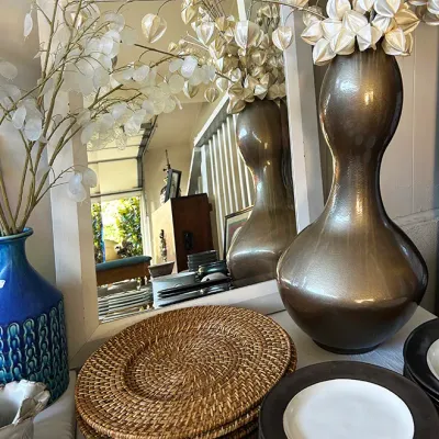 Sale Photo Thumbnail #286: Collection of tabletop decor, including woven rattan chargers, modern black and white rimmed ceramic plates, a bronze-tone gourd-shaped vase, and a blue textured ceramic vase with faux floral stems.
