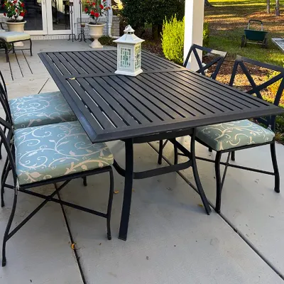 Sale Photo Thumbnail #220: Black slatted aluminum outdoor dining table set with four matching X-back chairs and light blue pattern cushions.