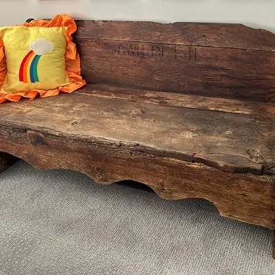 Sale Photo Thumbnail #22: Antique rustic wooden bench featuring carved lettering on the backrest and a scalloped apron, styled with a vintage yellow rainbow throw pillow.